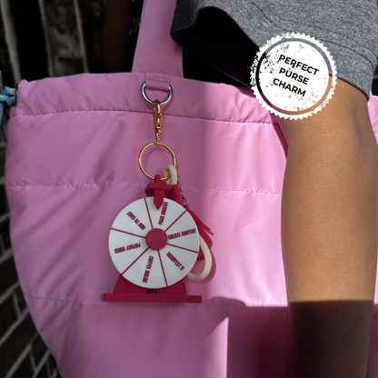 Pink bag with a keychain labeled 'Perfect Purse Charm' on a blurred background
